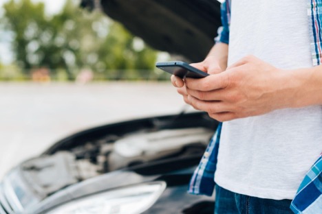 Person using a phone near a broken-down car.